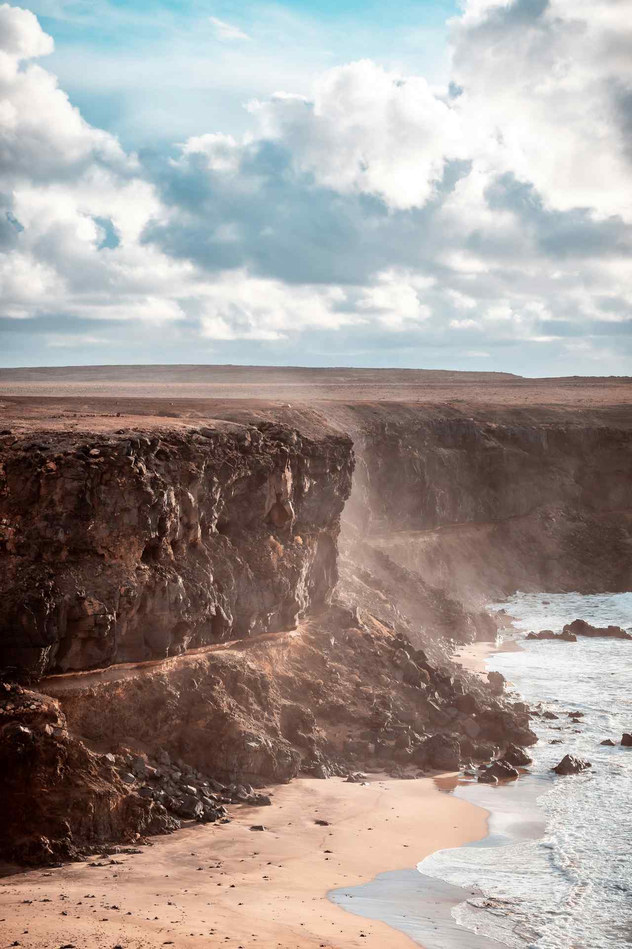 Steilküste mit Gischt und Wolkenhimmel